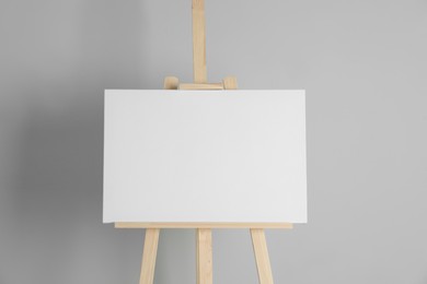 Photo of Wooden easel with blank canvas on light background