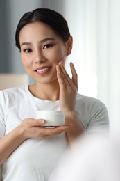Happy woman applying face cream at home