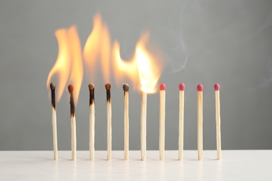 Line of burning and whole matches on table against grey background