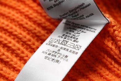 Photo of Clothing label with recommendations for care on orange garment, closeup