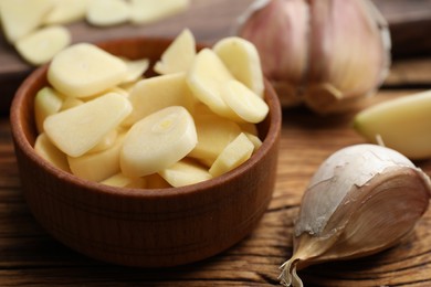 Photo of Fresh chopped garlic in bowl on wooden table, closeup. Organic product