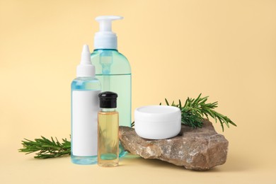 Photo of Bottles with cosmetic products, stone and rosemary on beige background