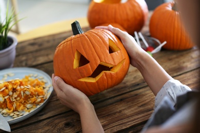 Photo of Woman with pumpkin jack o'lantern at wooden table, closeup. Halloween celebration