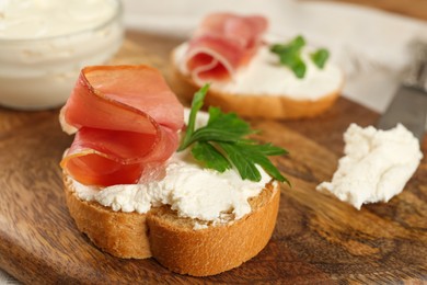 Photo of Delicious sandwiches with cream cheese and jamon on wooden board, closeup