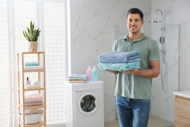 Photo of Happy man with clean towels in bathroom. Laundry day