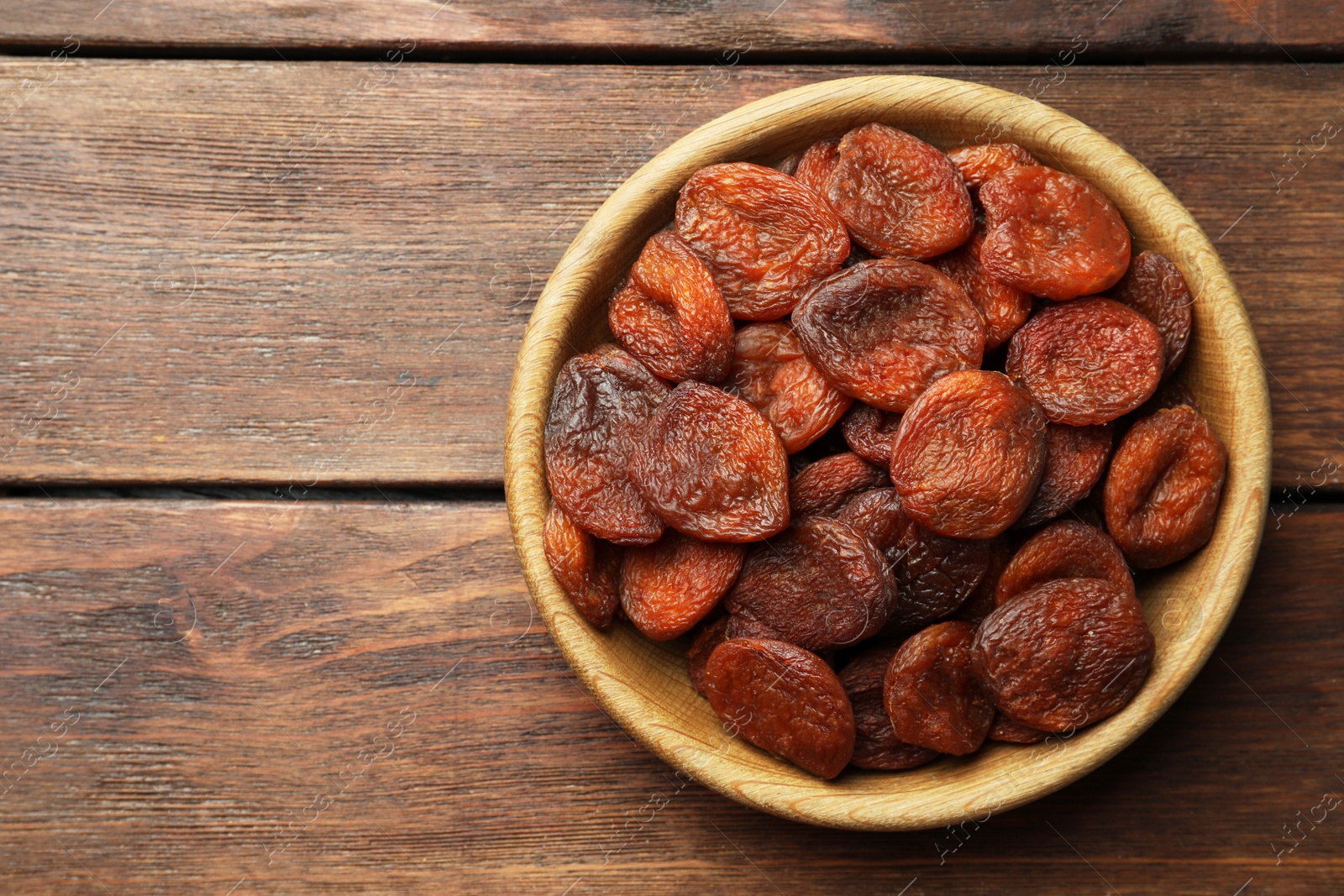 Photo of Bowl of tasty apricots on wooden table, top view and space for text. Dried fruits