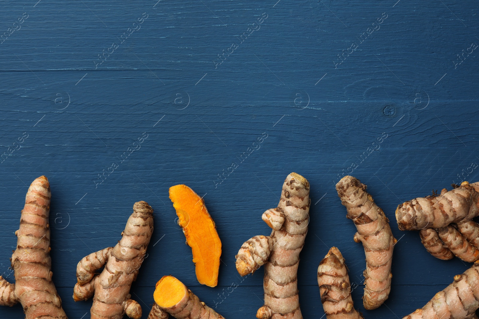 Photo of Whole and cut turmeric roots on blue wooden table, flat lay. Space for text