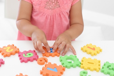 Little girl playing with colorful puzzles at white table, closeup. Educational toy