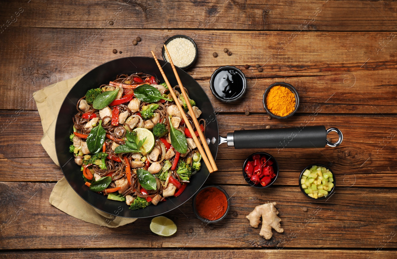 Photo of Stir-fry. Tasty noodles with meat in wok, chopsticks and ingredients on wooden table, flat lay