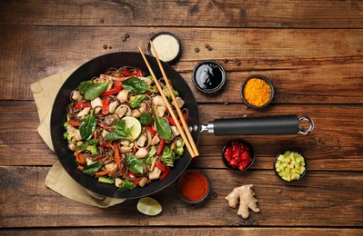 Stir-fry. Tasty noodles with meat in wok, chopsticks and ingredients on wooden table, flat lay