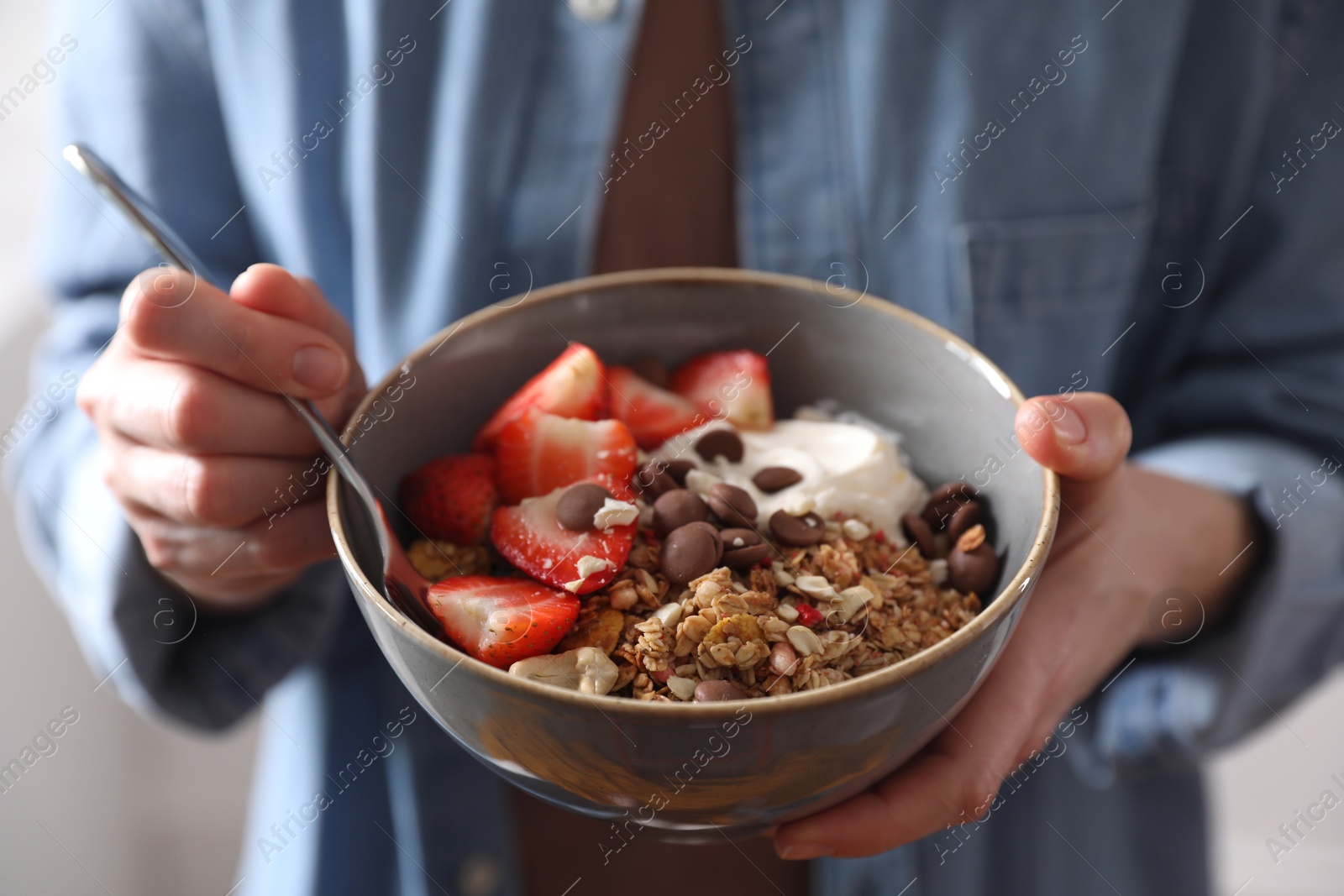 Photo of Woman eating tasty granola with chocolate chips, strawberries and yogurt, closeup