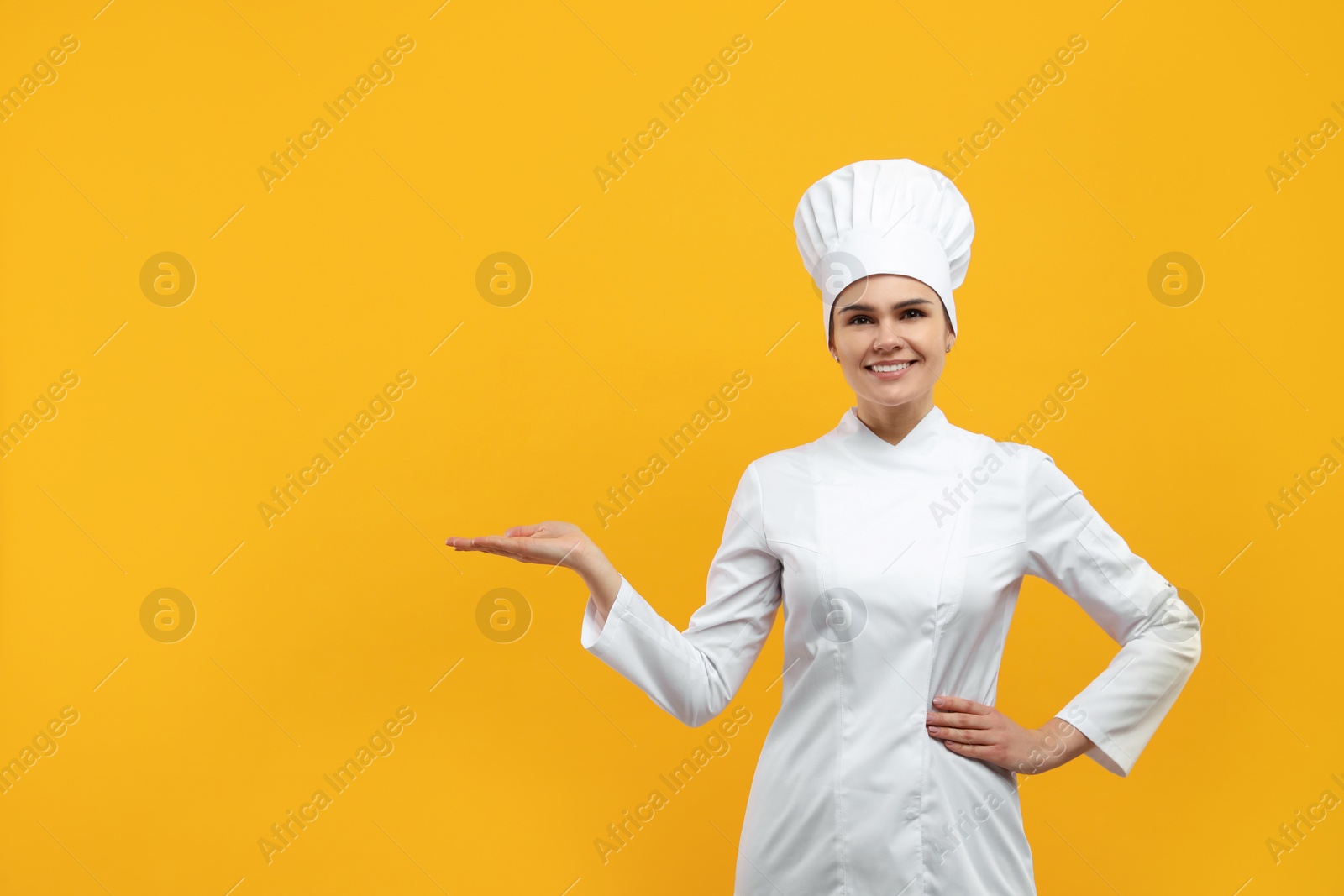 Photo of Happy female chef wearing uniform and cap on orange background. Space for text