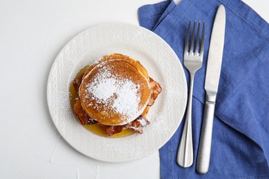 Delicious pancakes with maple syrup, sugar powder and fried bacon on white table, flat lay