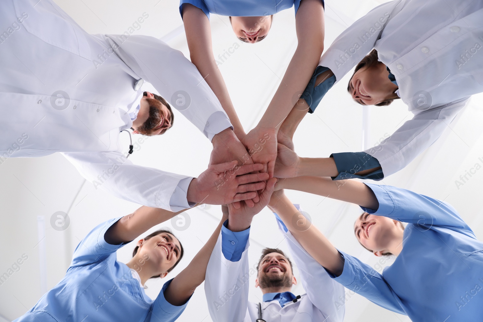 Photo of Team of medical doctors putting hands together indoors, bottom view