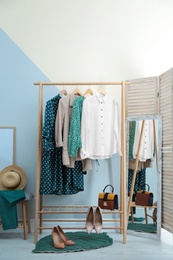 Photo of Wardrobe rack with women's clothes and shoes at color wall in room