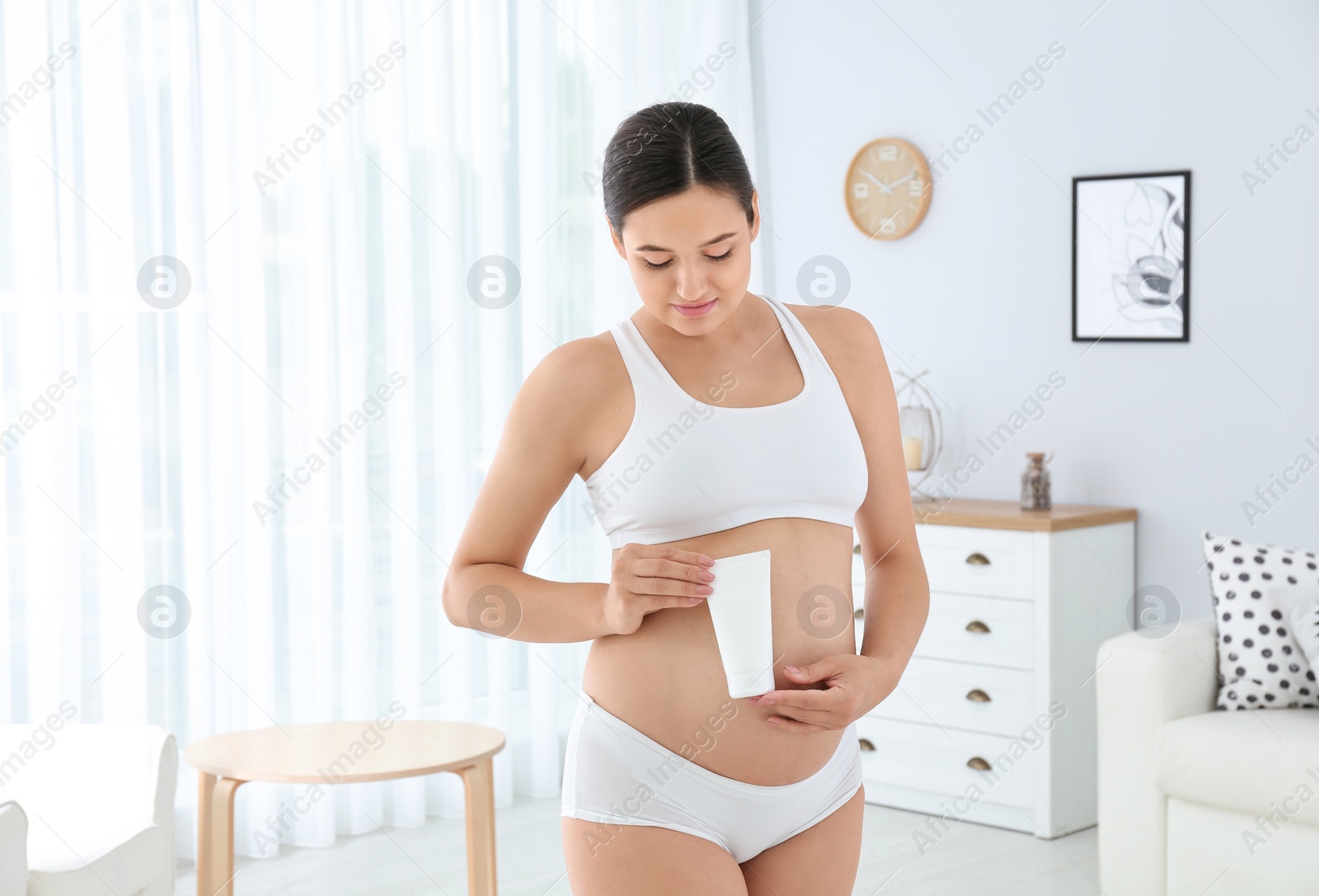 Photo of Pregnant woman holding body cream at home