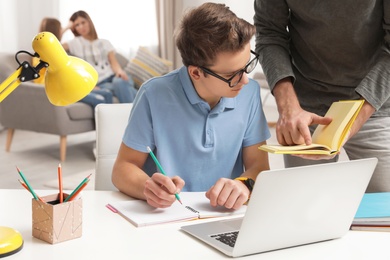 Father helping his teenager son with homework indoors