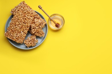 Puffed rice bars (kozinaki) and honey on yellow background, flat lay. Space for text