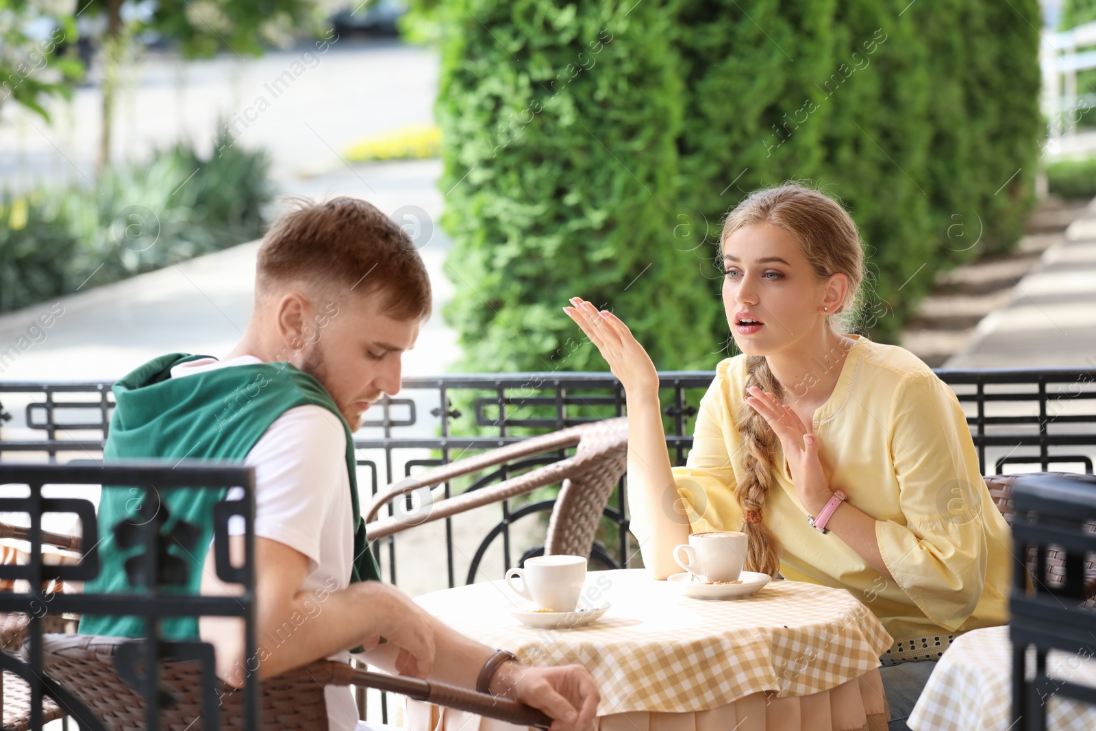 Photo of Young couple arguing while sitting in cafe, outdoors. Problems in relationship