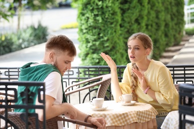 Young couple arguing while sitting in cafe, outdoors. Problems in relationship