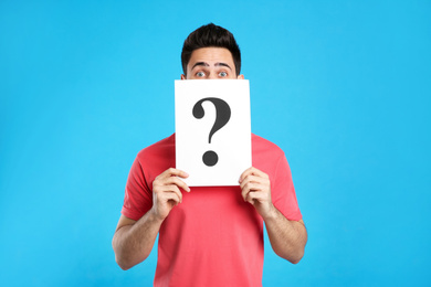 Photo of Emotional young man with question mark sign on light blue background