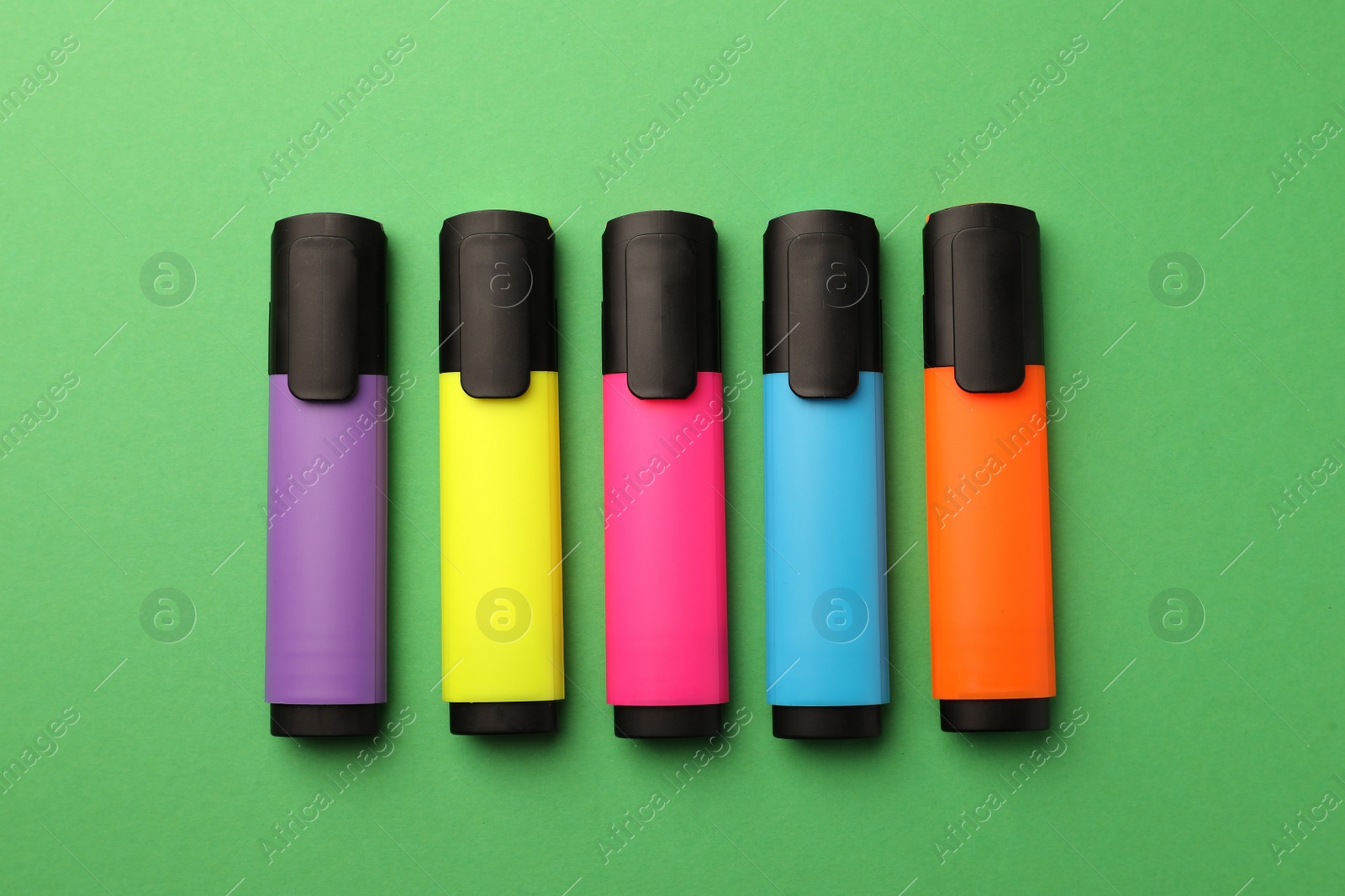 Photo of Bright color markers on green background, flat lay