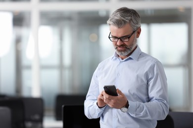 Handsome man with smartphone in office, space for text. Lawyer, businessman, accountant or manager