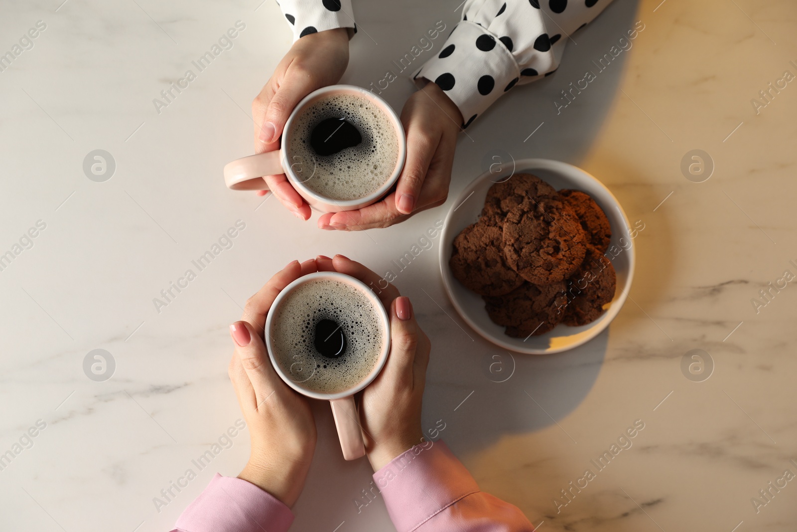 Photo of Women with cups of hot coffee and cookies at white marble table, top view