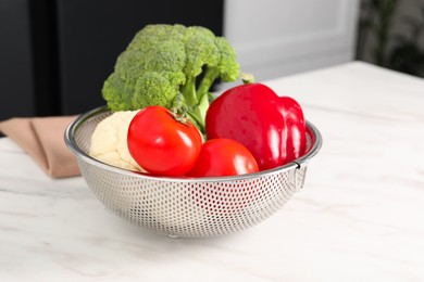 Photo of Colander with different fresh vegetables on white table indoors