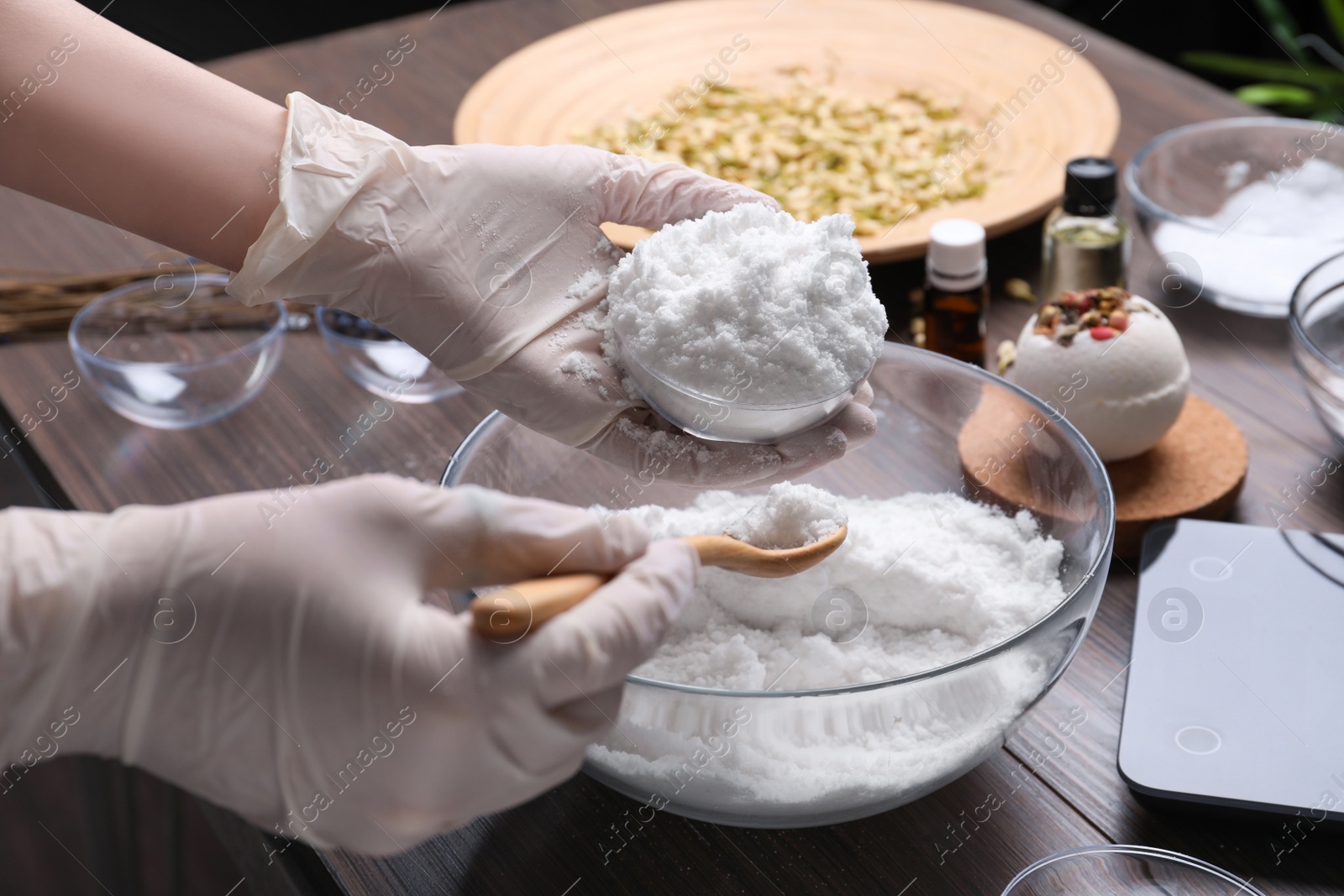 Photo of Woman in gloves making bath bomb at wooden table, closeup