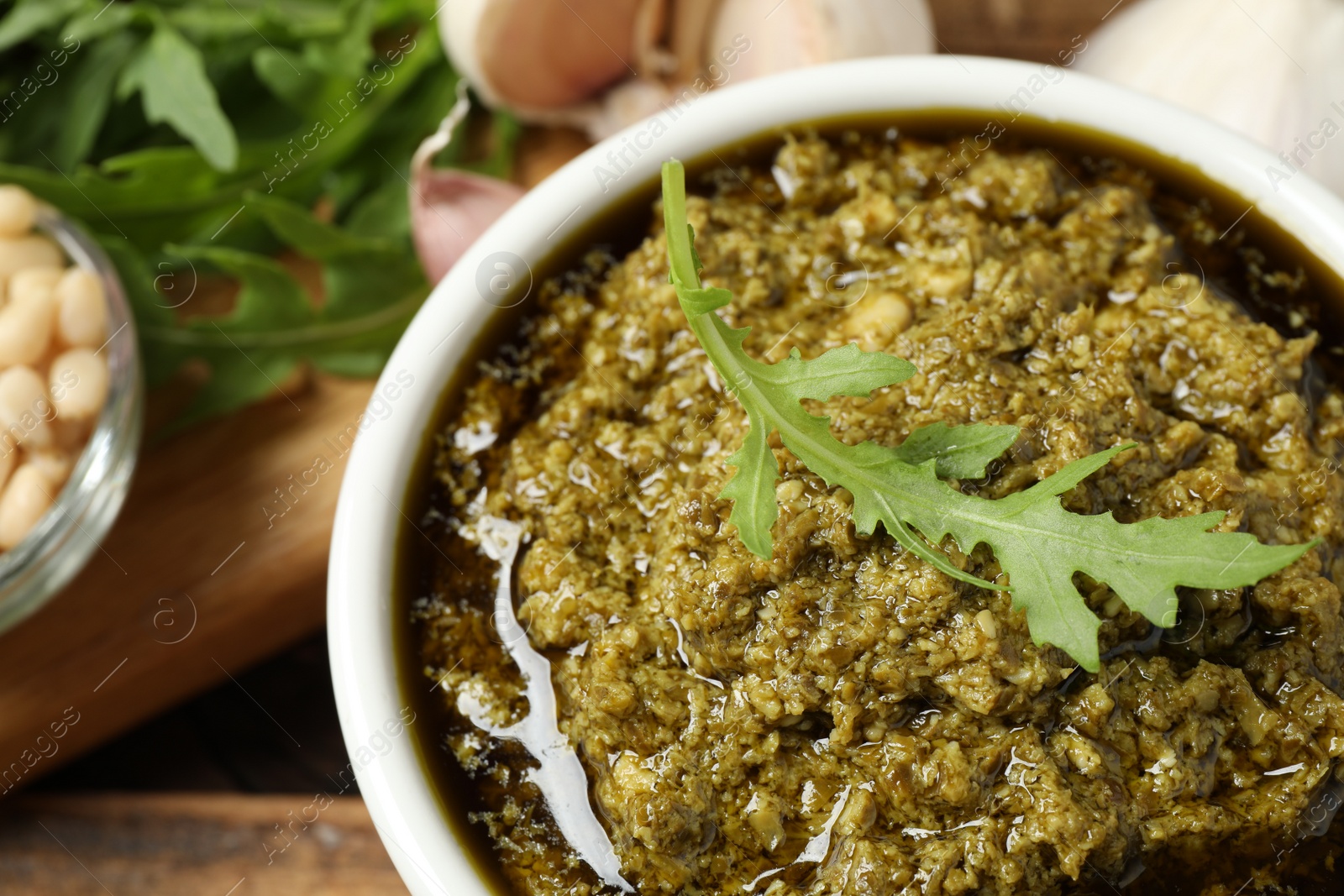 Photo of Bowl of tasty arugula pesto on table, closeup