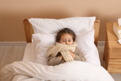 Photo of Sick girl with scarf around neck lying in bed at home, above view
