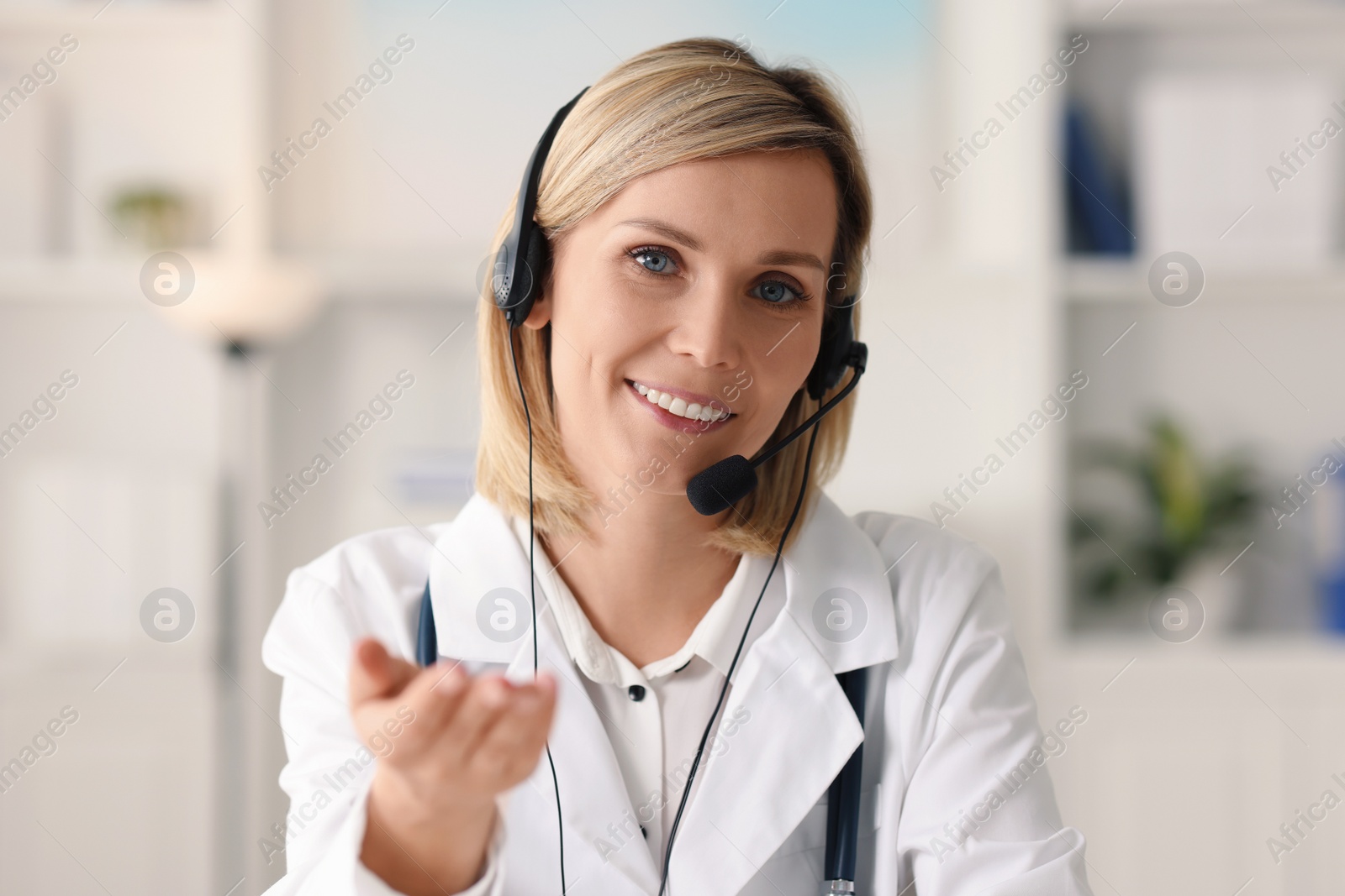 Photo of Portrait of smiling doctor in headphones having online consultation indoors