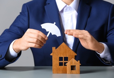 Photo of Man covering wooden houses with umbrella cutout at table, closeup. Home insurance