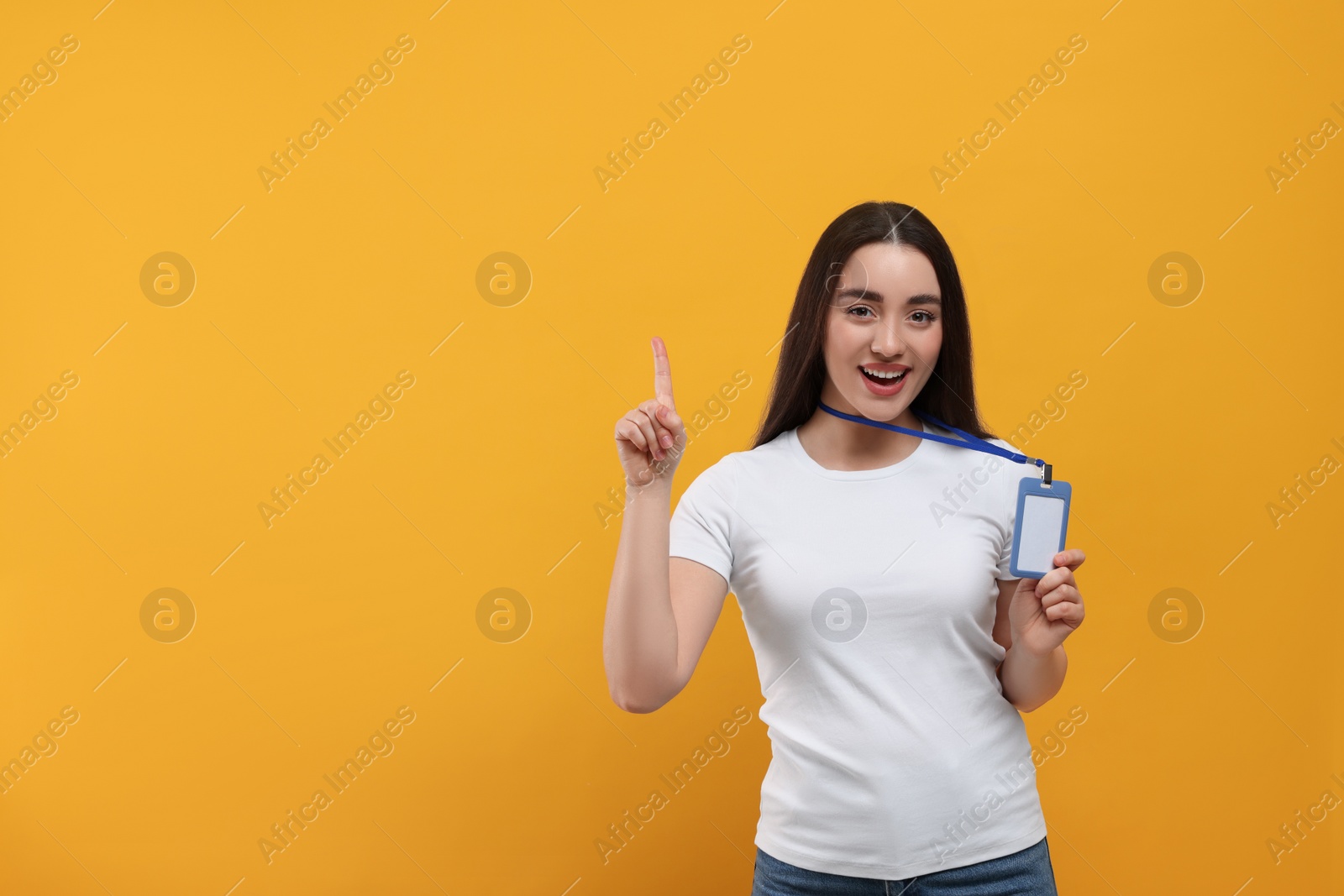 Photo of Smiling woman holding vip pass badge and pointing at something on orange background. Space for text