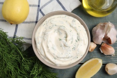 Photo of Tasty creamy dill sauce and ingredients on blue wooden table, flat lay