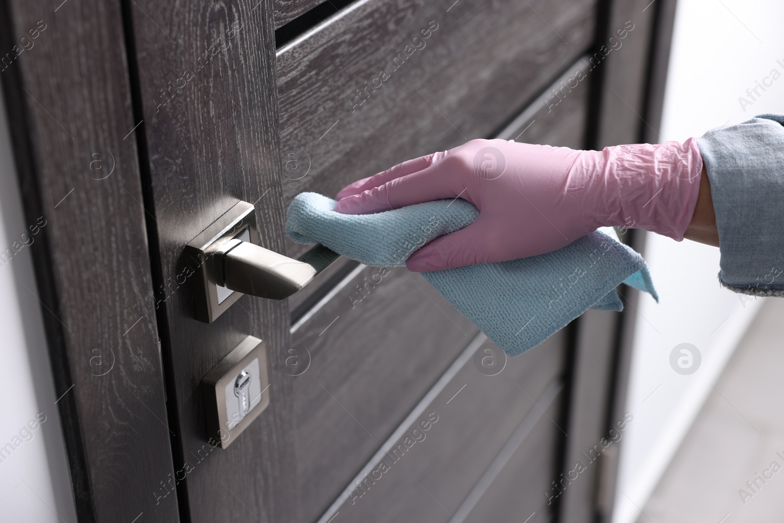 Photo of Woman wiping door handle with rag indoors, closeup