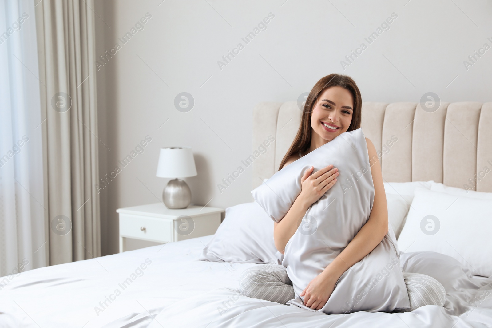 Photo of Young woman hugging pillow on comfortable bed with silky linens