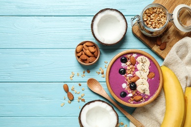 Photo of Delicious acai smoothie with granola and almonds served on light blue wooden table, flat lay. Space for text