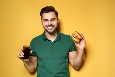 Handsome man with tasty burger and cola on color background