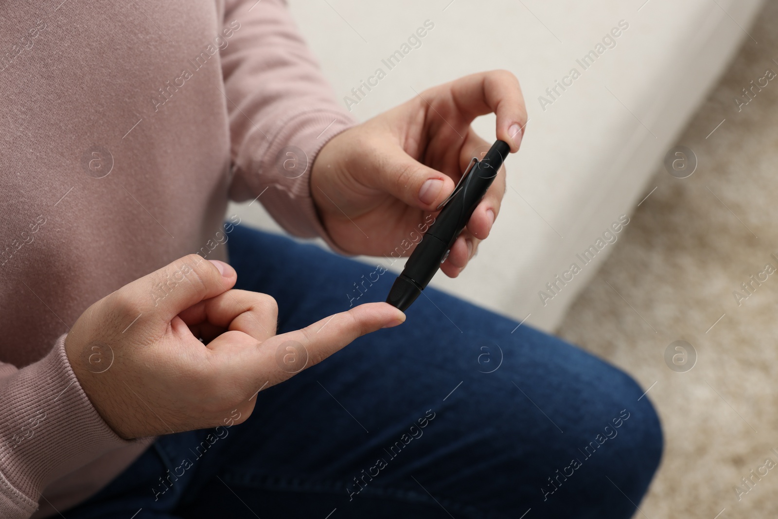 Photo of Diabetes test. Man checking blood sugar level with lancet pen at home, closeup