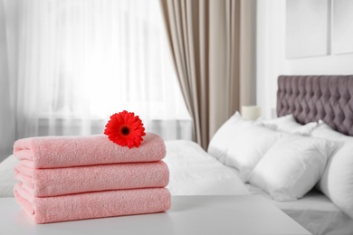 Stack of fresh towels with flower on table in bedroom. Space for text