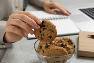 Photo of Office worker taking chocolate chip cookie from bowl at light gray table indoors, closeup