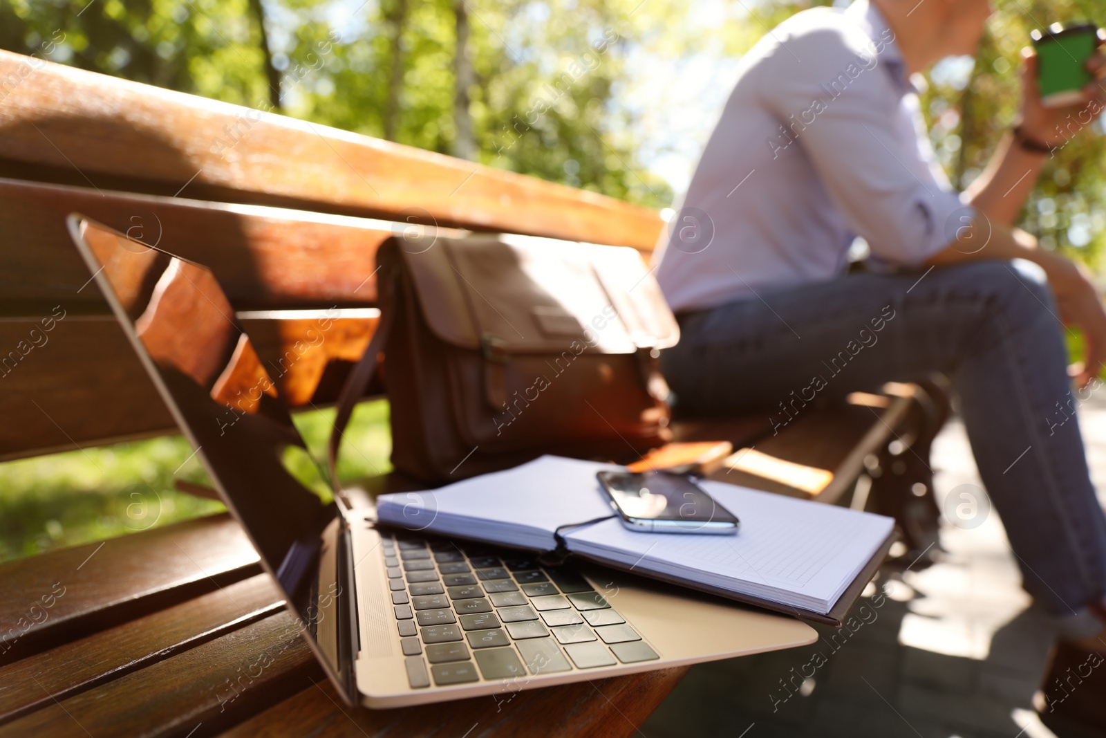 Photo of Man taking coffee break during work in park, focus on laptop