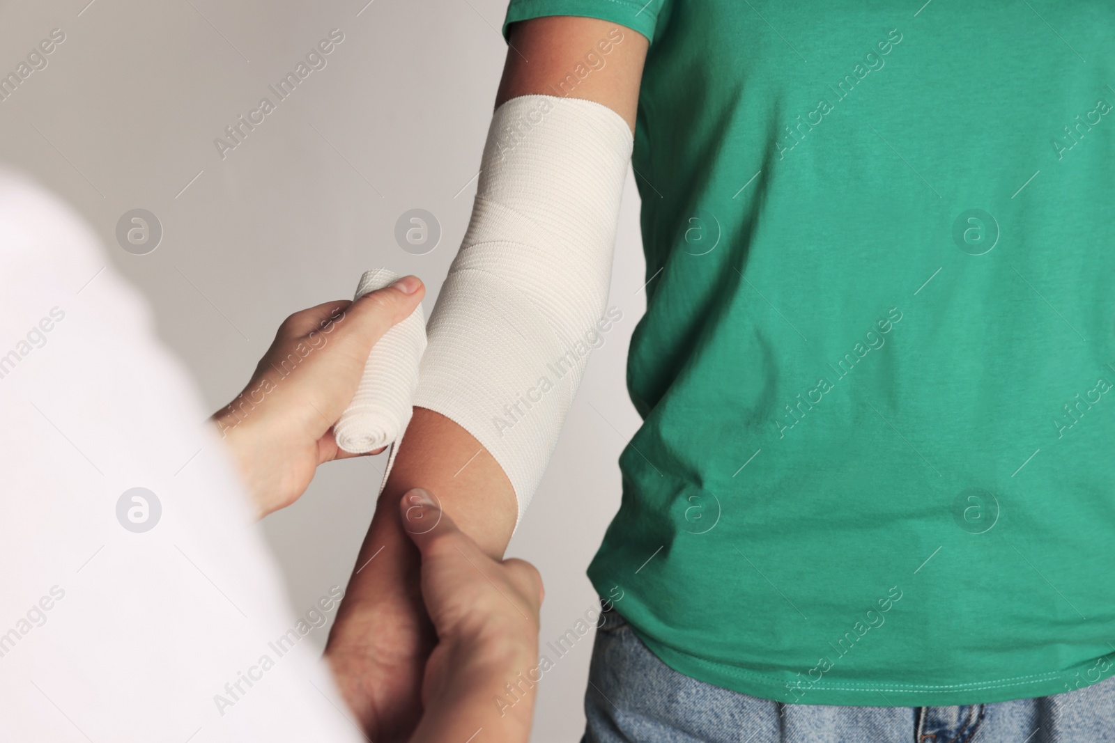 Photo of Doctor applying bandage onto patient's arm on grey background, closeup