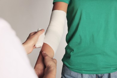 Photo of Doctor applying bandage onto patient's arm on grey background, closeup