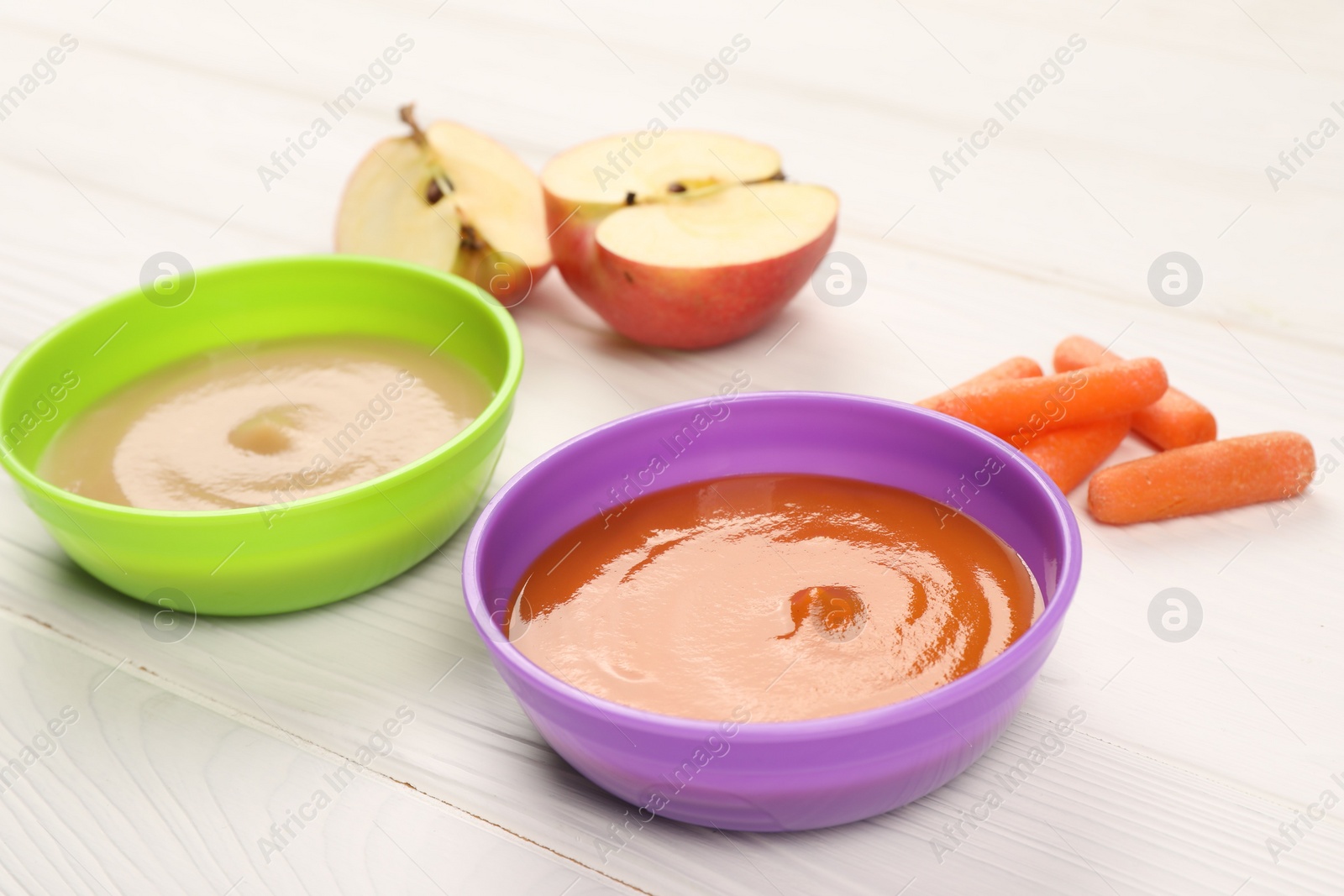 Photo of Baby food. Purees of apples and carrots in bowls on white wooden table