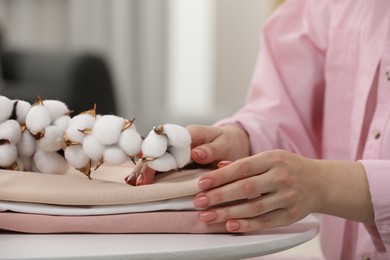 Photo of Woman touching bed sheets and cotton branch with fluffy flowers at white table in room, closeup