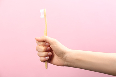 Woman holding bamboo toothbrush on pink background, closeup