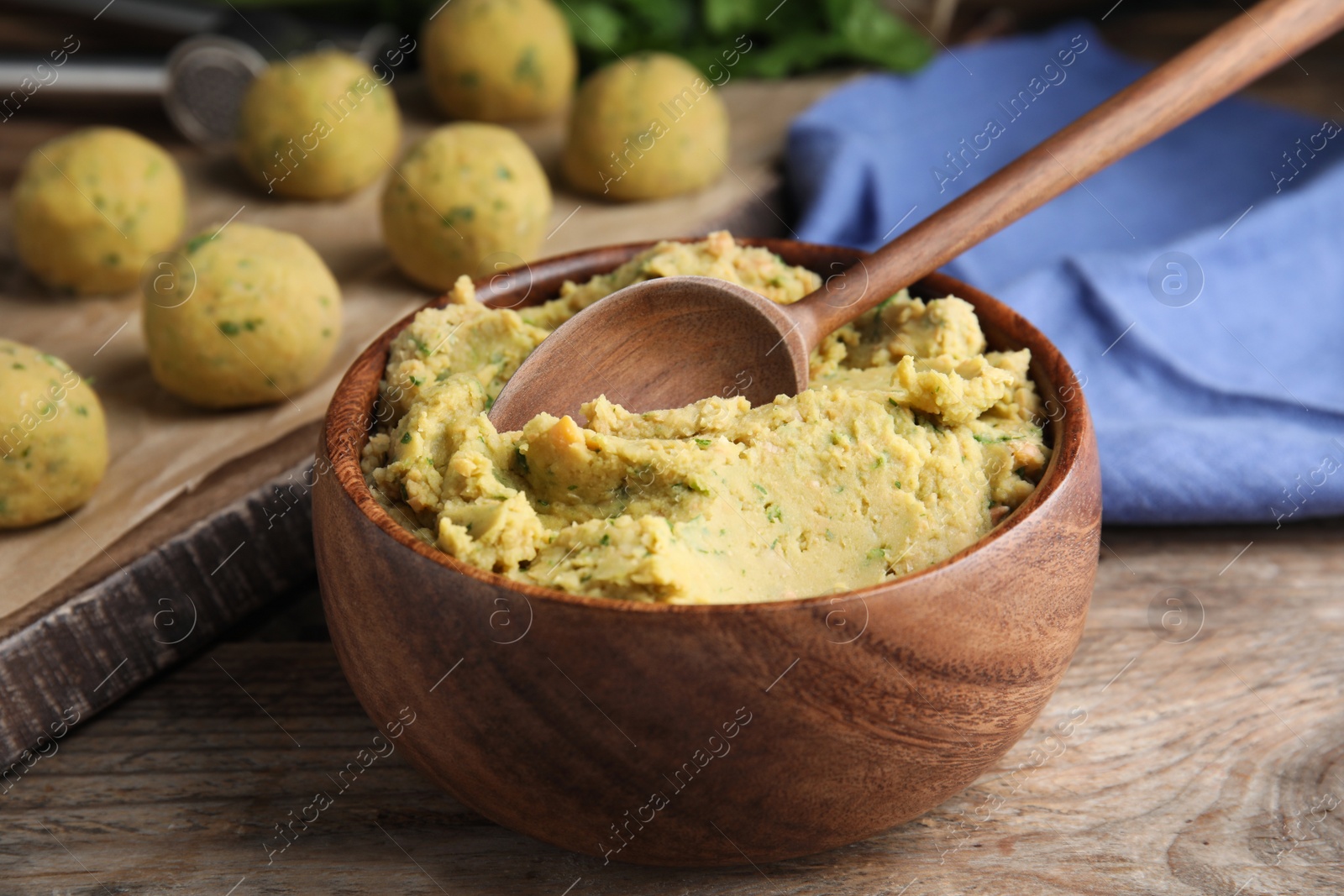 Photo of Bowl of chickpea puree with spoon on wooden table. Falafel recipe